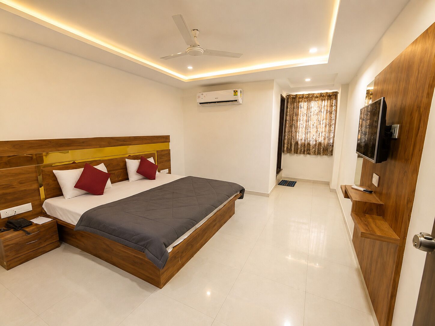 A modern bedroom with a wooden bed, a ceiling fan, an air conditioning unit, and a TV mounted on the wall.