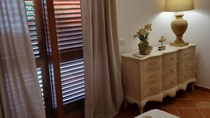 Ein Schlafzimmer mit Bett, Schminktisch, Lampe und einem Fenster mit Jalousien.