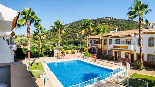 A swimming pool with a surrounding deck, palm trees, and buildings in the background. - Lovely home in Benaojan with swimming pool (Benaojan)
