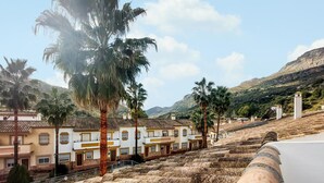 A hillside residential area with terraced stone structures, palm trees, and traditional buildings with tiled roofs. - Lovely home in Benaojan with swimming pool (Benaojan)