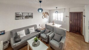 A living room with a grey sofa, two armchairs, a white coffee table with a plant, and a dining area with a table and chairs. - Lovely home in Benaojan with swimming pool (Benaojan)