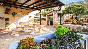 Eine Terrasse im Freien mit Steintischen und -bänken, umgeben von Topfpflanzen und einer Steinmauer.