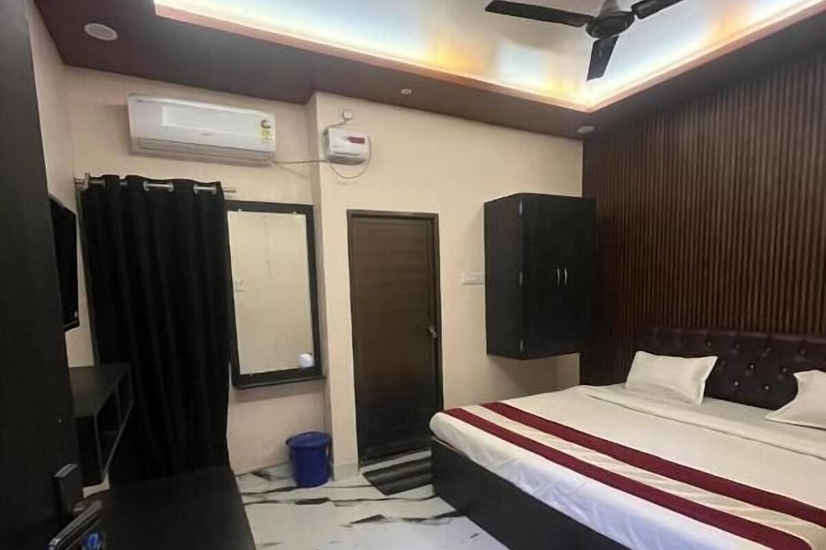 Una habitación de hotel con cama, ventilador de techo, aire acondicionado, espejo, puerta y una pequeña mesa.