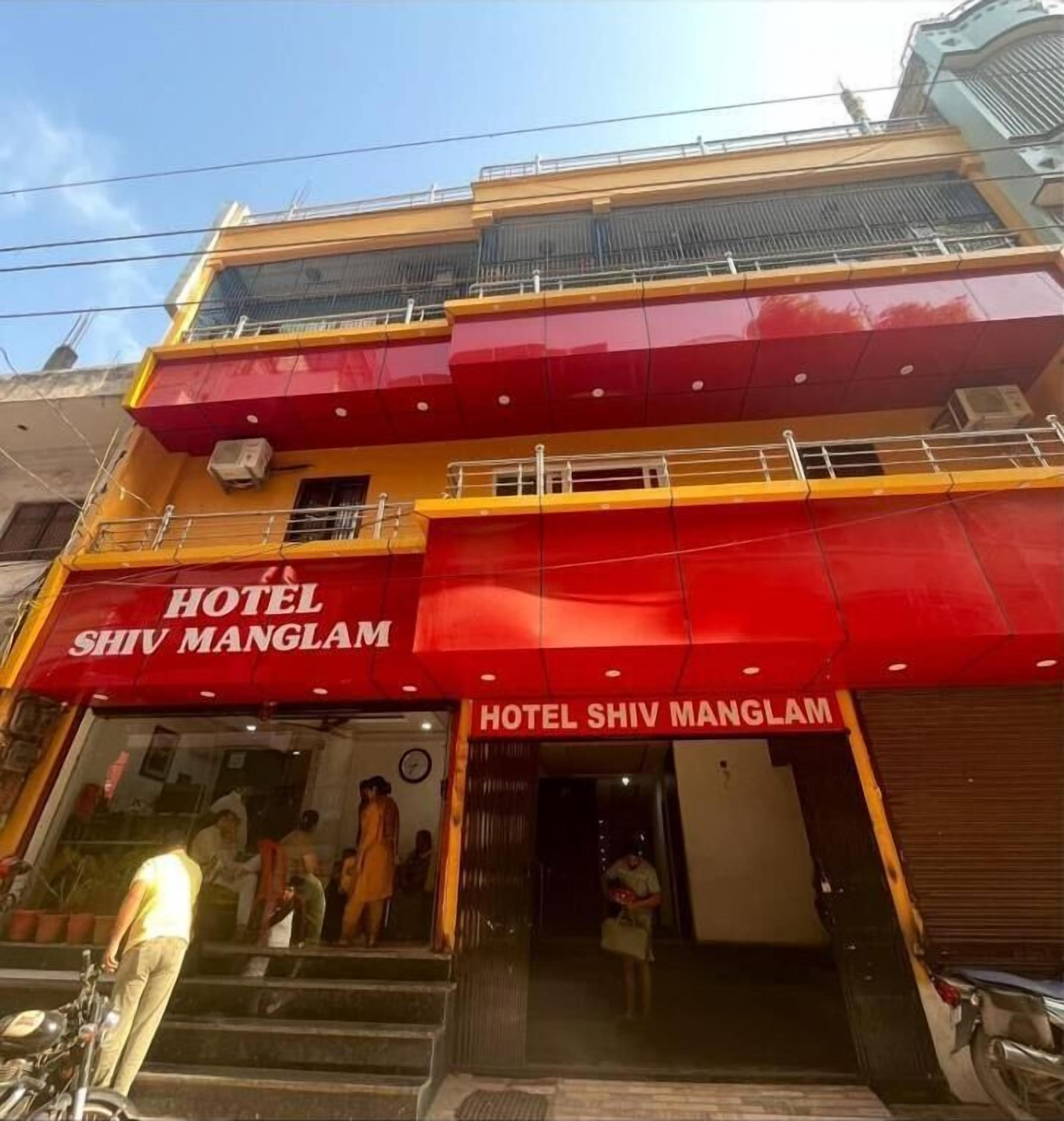 A hotel named 'Hotel Shiv Manglam' with a red and yellow facade, a visible entrance, and a staircase leading to the entrance.