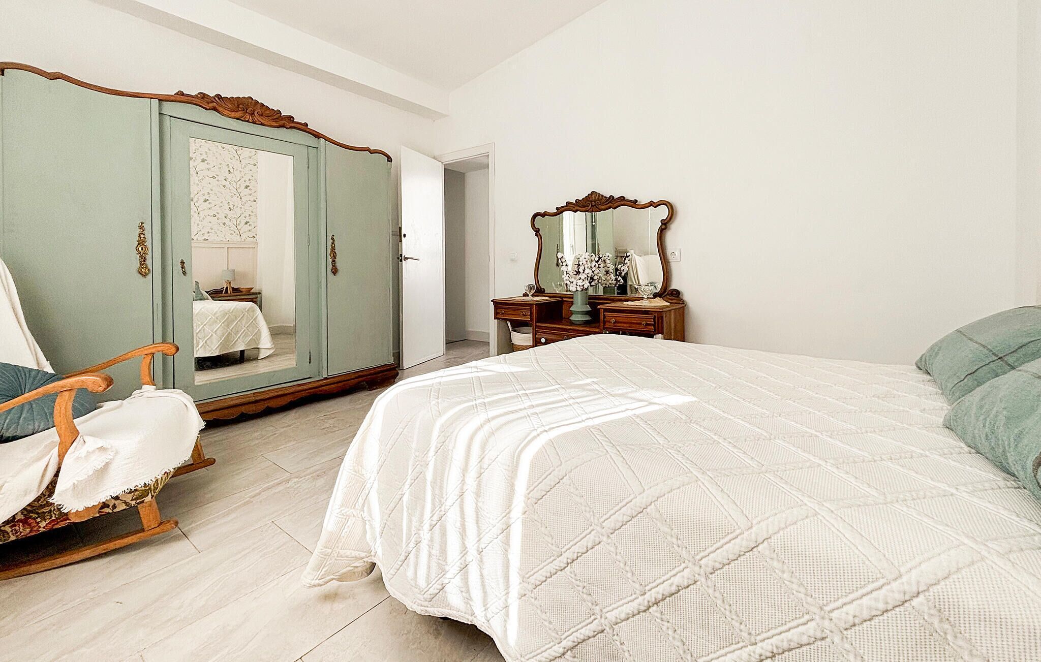 Een slaapkamer met een bed, een kledingkast, een stoel, een dressoir en een spiegel.
