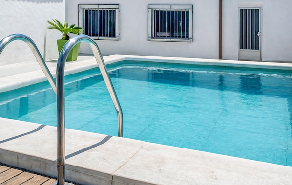 A swimming pool with a metal ladder, a potted plant, and a white building with barred windows.