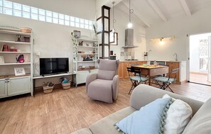 Ein modernes Wohnzimmer mit Flachbildfernseher, einem bequemen Sessel, einer Couch und einem Essbereich mit Tisch und Stühlen.