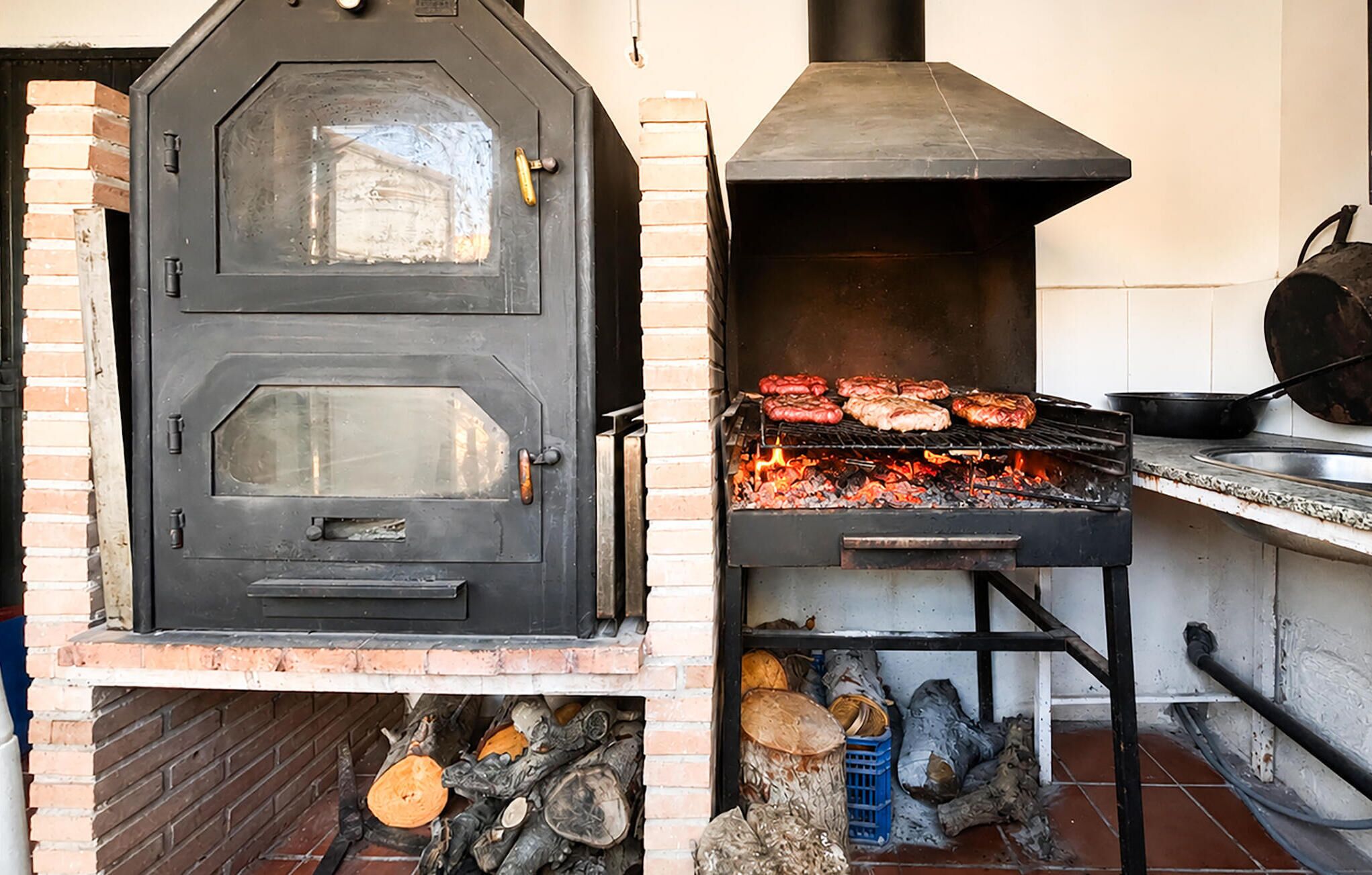 A brick oven with a black door and a grill with meat cooking.