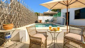 A poolside area with wicker chairs, a table with drinks, and a bamboo fence.