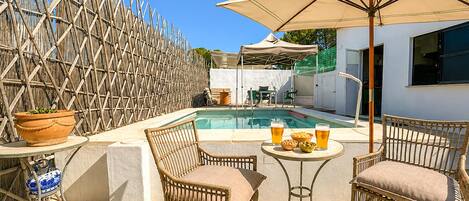 A poolside area with wicker chairs, a table with drinks, and a bamboo fence.