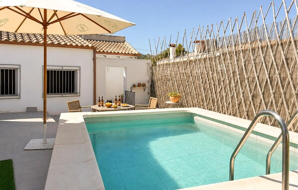 A swimming pool with a metal ladder, surrounded by a white wall and a bamboo fence.