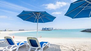 Una spiaggia con due ombrelloni blu e due lettini bianchi.