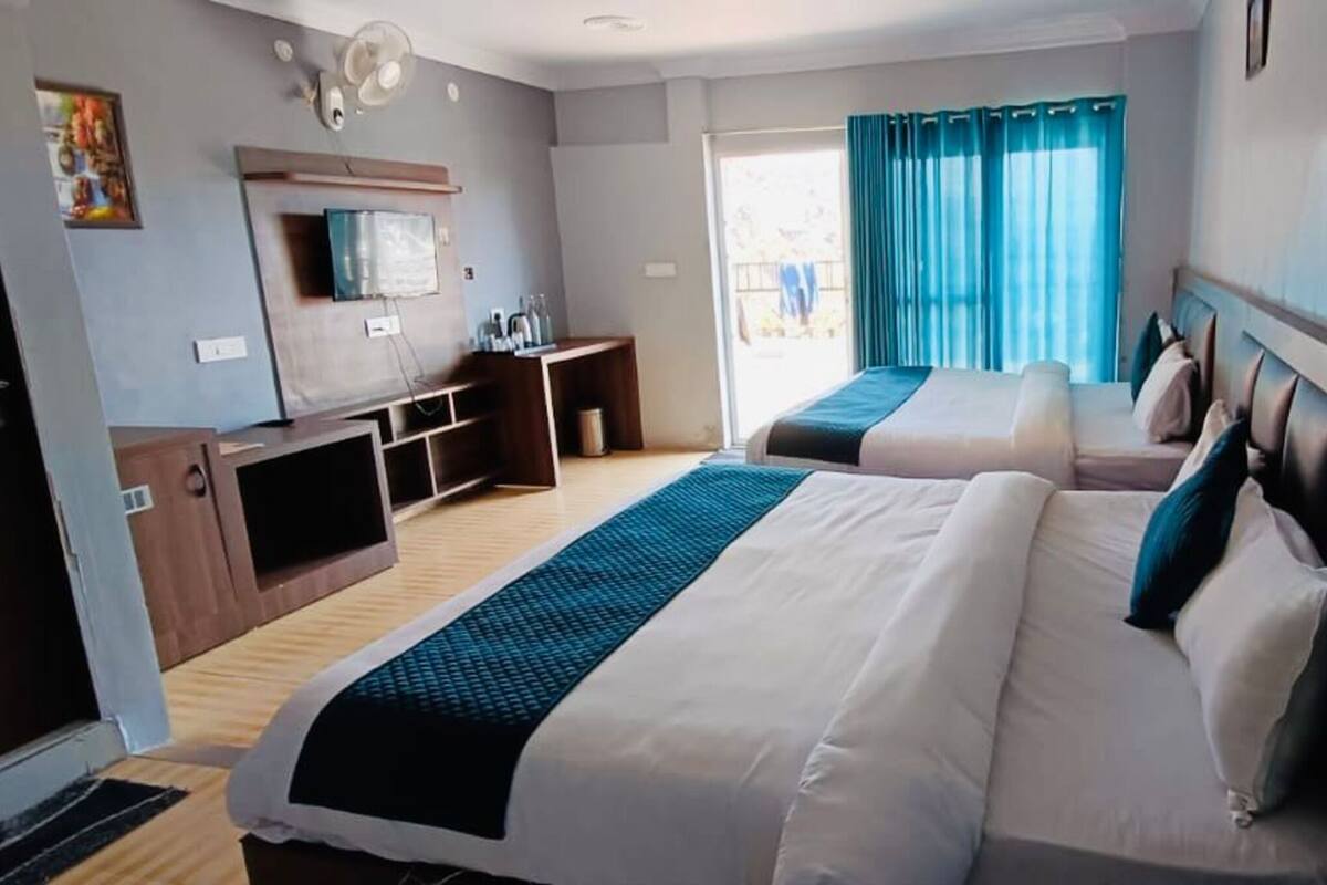 Een hotelkamer met twee bedden, een bureau met een computer, een televisie en een raam met gordijnen.