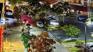 A hotel with multiple floors, a parking area, and a street with cars and pedestrians. - Cozy & Safe Island Studio Suite (Garapan)