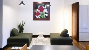 A modern dining room with a large table, two green sofas, a ceiling fan, pendant lights, a framed floral artwork, and a potted plant. - Cozy & Safe Island Studio Suite (Garapan)