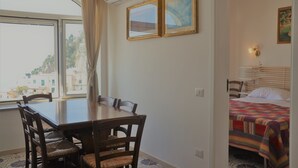 Une pièce comprenant une table à manger et des chaises, un lit recouvert d’une couverture colorée, et deux tableaux encadrés accrochés au mur.