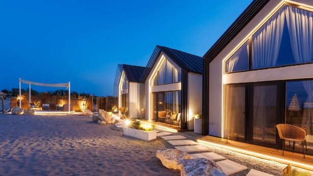 A beachfront hotel with modern architecture, featuring large windows and a well-lit outdoor area with seating. - OASIS VILLAGE (Eforie Nord)