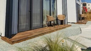 A modern two-story house with large sliding glass doors, a wooden deck, and a small outdoor seating area with chairs. - OASIS VILLAGE (Eforie Nord)