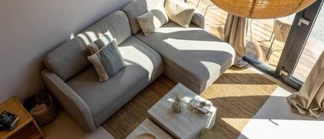 A modern living room with a grey sofa, two side tables, and a large window providing natural light.