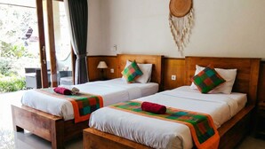 Two wooden beds with white linens and colorful blankets, a woven wall hanging, and a view of greenery outside. - Putu's Paradise Ubud (Ubud)