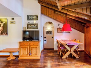 Ein Holztisch mit kariertem Tischläufer, ein Fernseher auf einer Holzkommode und gerahmte Bilder an der Wand.