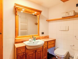 Ein Badezimmer mit einem Holzkonsolenunterschrank, einem Spiegel, einem Waschbecken und einer Toilette.