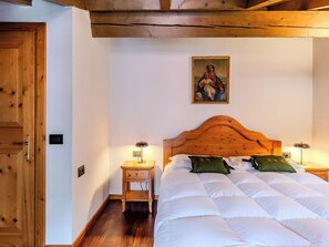 Ein Schlafzimmer mit einem hölzernen Kopfende, einem Bett mit weißer Bettwäsche, zwei Nachttischen mit Lampen und einem religiösen Gemälde an der Wand.