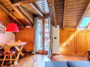 A wooden interior with a dining table, chairs, a red lamp, and a sliding door leading to an outdoor area. - Mansarda al Campanile by Interhome (Pinzolo)