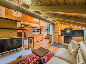 A cozy cabin interior with a wooden ceiling, a TV, a sofa, a kitchen area, and a dining table. - Mansarda San Lorenzo by Interhome (Pinzolo)