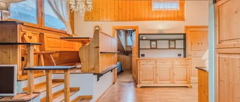 Interior de madera con una escalera, una zona de cocina y vistas por una ventana.