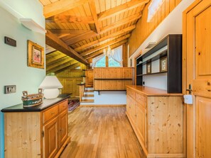 A wooden interior with a staircase leading to a loft bedroom, built-in shelves, and a chandelier. - Mansarda San Lorenzo by Interhome (Pinzolo)