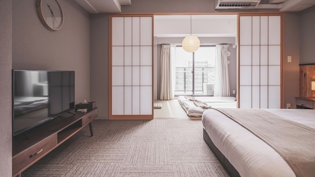 Habitación de hotel moderna con una cama grande, un televisor de pantalla plana, una puerta corrediza de estilo shoji y vistas a la ciudad.