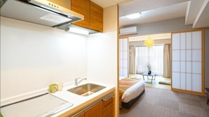 Una habitación de hotel compacta con kitchenette, una cama, una mesita y una puerta corredera tradicional.