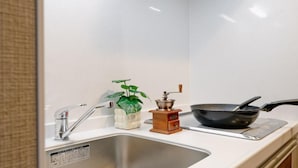Una cocina con un lavamanos de acero inoxidable, una sartén negra sobre una estufa, una planta blanca en una maceta decorativa y un molinillo de especias de madera.