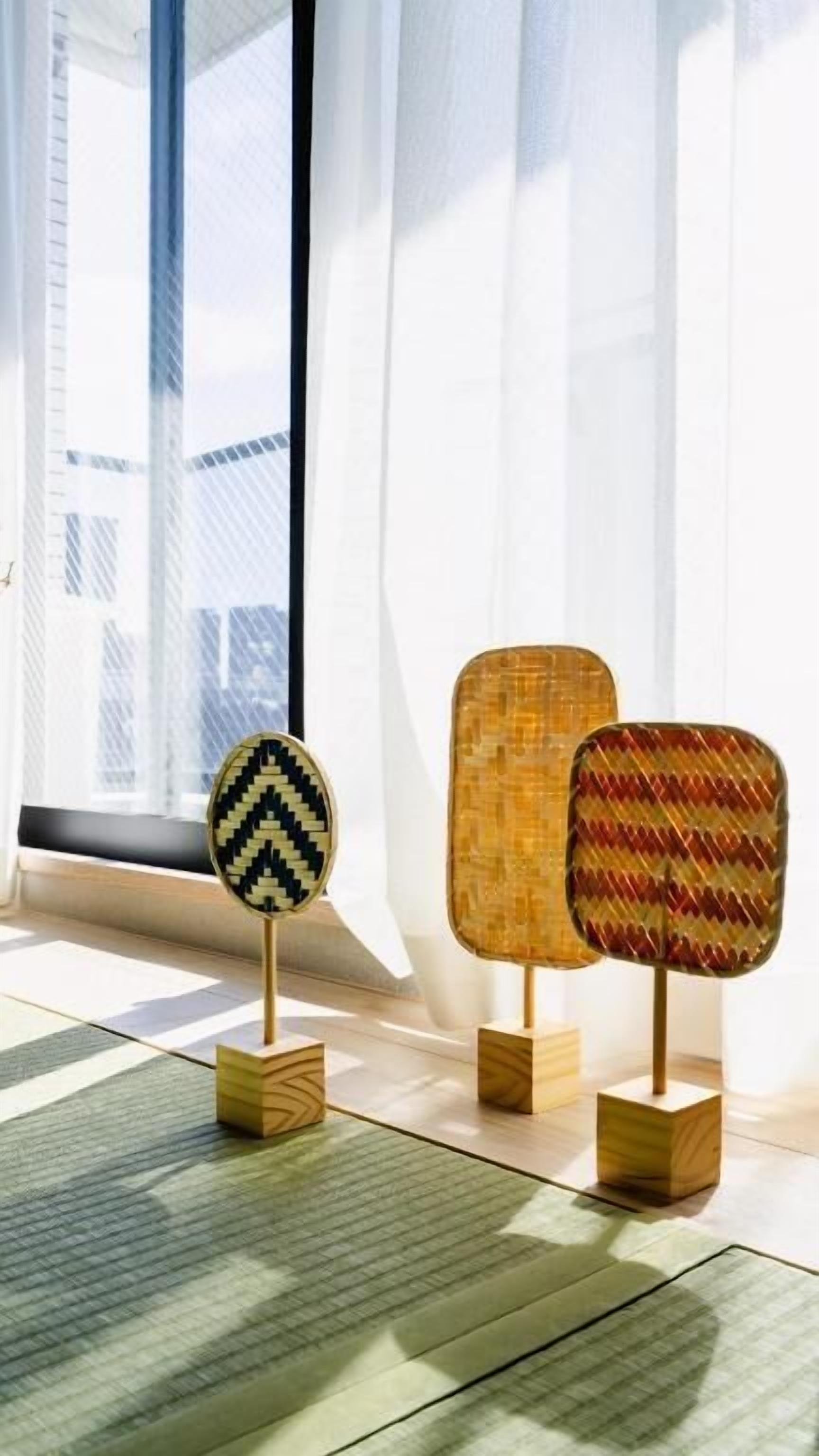 Three decorative panels with geometric patterns, each mounted on a wooden base, displayed in a room with a large window and sheer curtains.