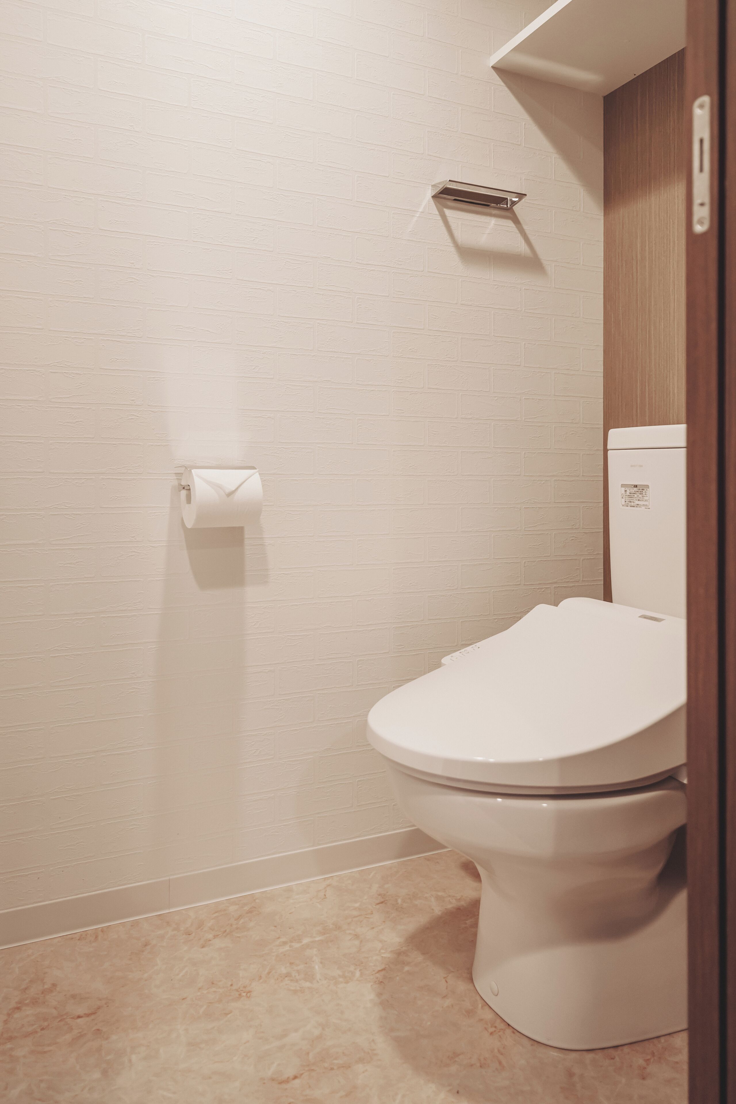 A bathroom with a white toilet, a paper towel dispenser, and a marble floor.