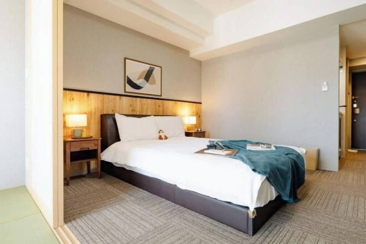 A hotel room with a bed, nightstands, a lamp, a framed picture, and a carpeted floor.