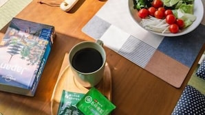 Una mesa de desayuno ordenada con una ensalada, una taza de café y un libro.