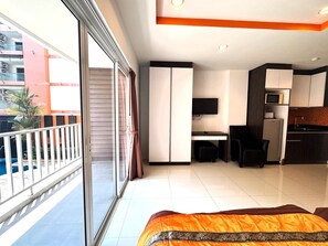 A modern hotel room with a balcony, a desk, a TV, a refrigerator, and a kitchen area. - Cozy Pool-view Studio With Balcony - New Nordic VIP 3, Pratumnak (Pattaya)