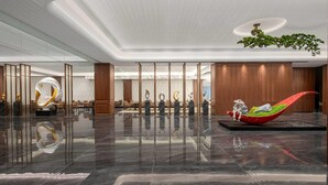 Un lobby moderno de hotel con un piso de mármol pulido, un mostrador de recepción y una escultura singular de un barco rojo.
