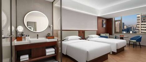 A modern hotel room with two beds, a bathroom with a vanity, and a city view.