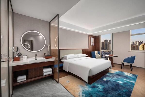 Une chambre d’hôtel moderne dotée d’un grand lit, d’une salle de bain avec un meuble-lavabo, d’un bureau et offrant une vue sur la ville.