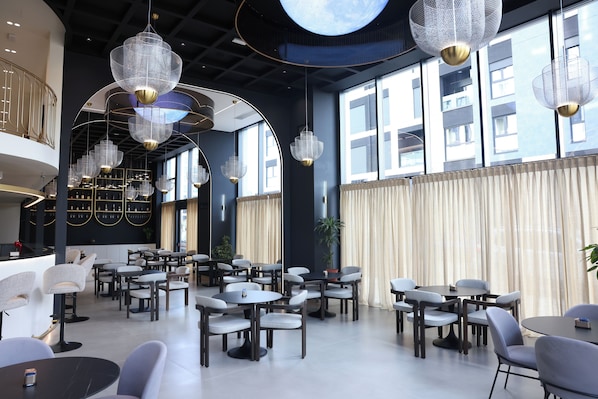A spacious dining area with multiple tables and chairs, large windows, and hanging chandeliers. - Mece Hotel (Tirana)