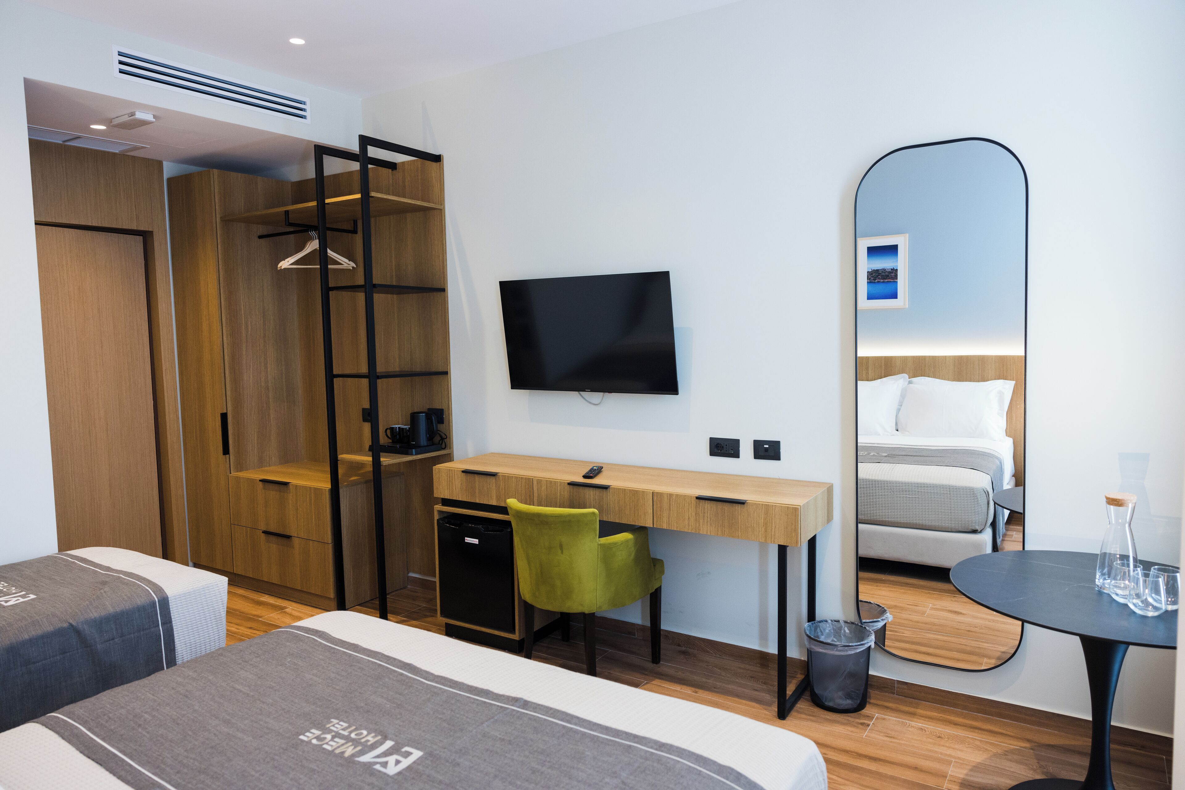 Hotelkamer met een houten garderobe, bureau met stoel, bed met hoofdeinde, tv aan de muur en een klein tafeltje met glazen.