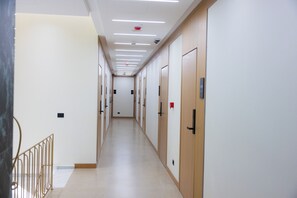 A long, narrow hallway with doors on one side and a metal railing on the other. - Mece Hotel (Tirana)