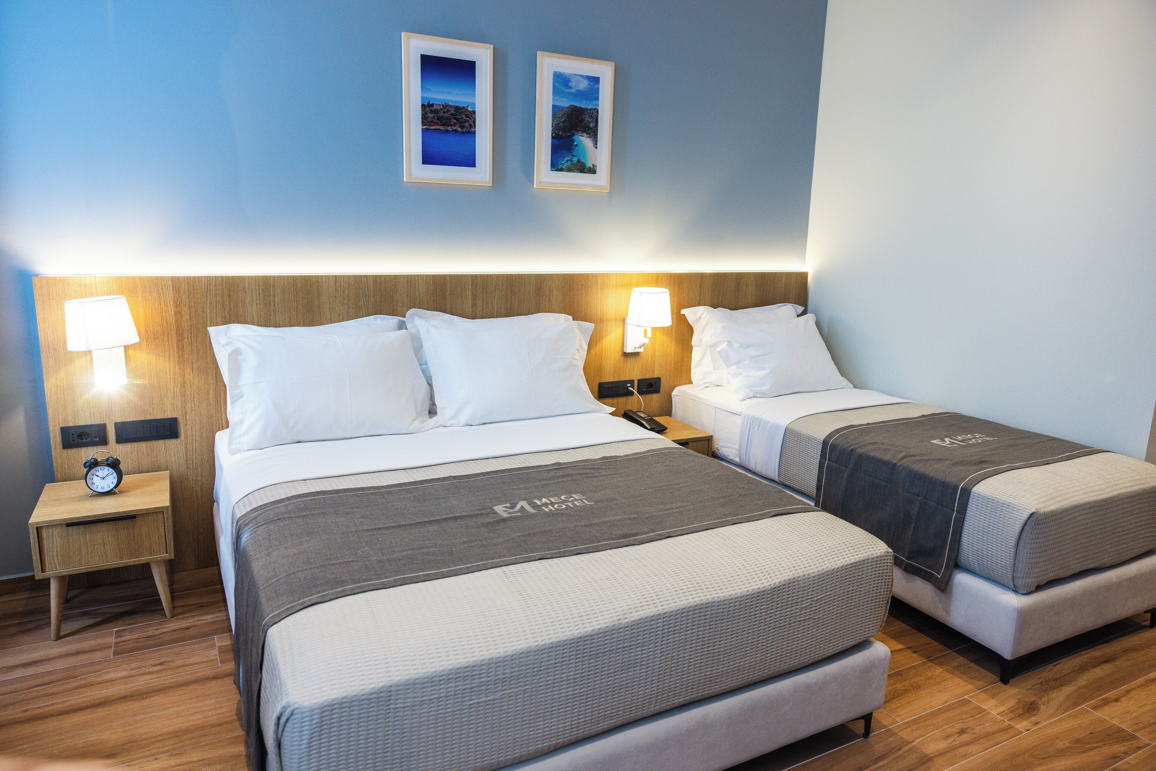 A hotel room with two beds, a nightstand with a clock, and wall-mounted lamps.