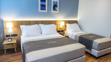 A hotel room with two beds, a nightstand with a clock, and wall-mounted lamps.
