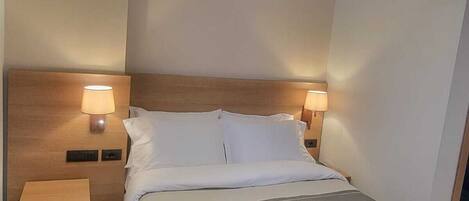 A modern hotel room with a neatly made bed, two bedside tables with lamps, and a clean, minimalist design.