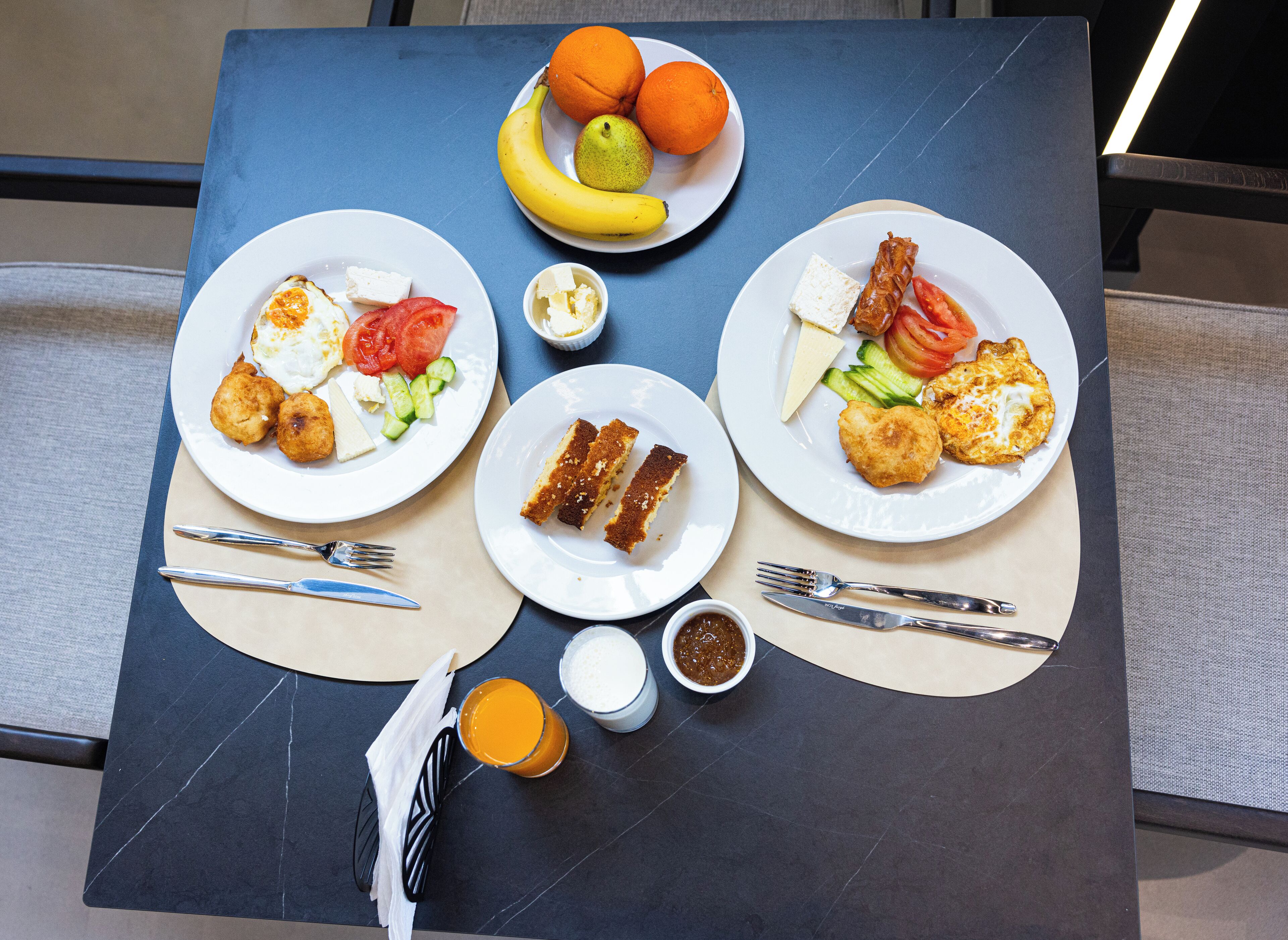Una mesa con platos de desayuno, cubiertos y un frutero.