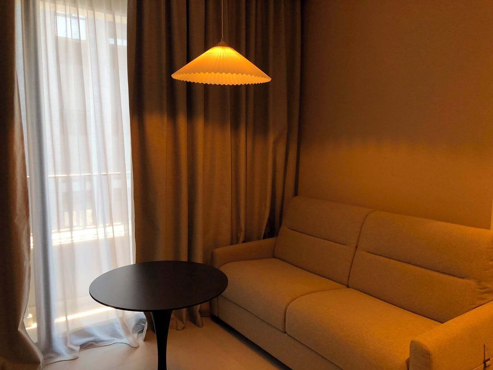 A room with a sofa, a round table, and a hanging lamp.